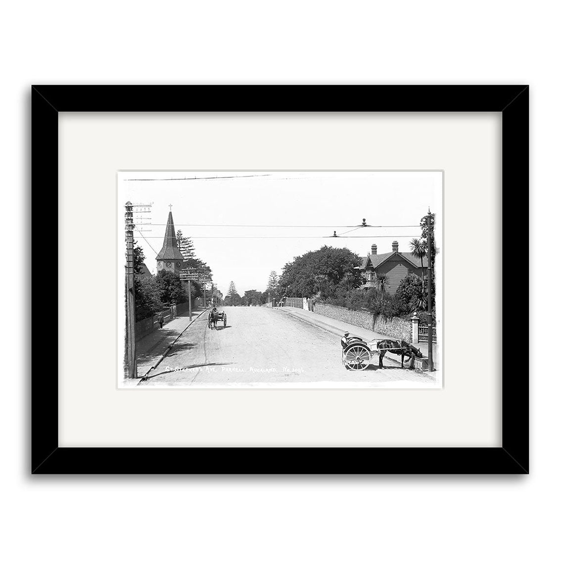 St Stephens Ave Parnell 1910 – HI051: Black and white historical photo print of a quiet New Zealand street with a horse-drawn cart, bicycle, trees, buildings, and church steeple. Framed in black with white mat; archival quality.