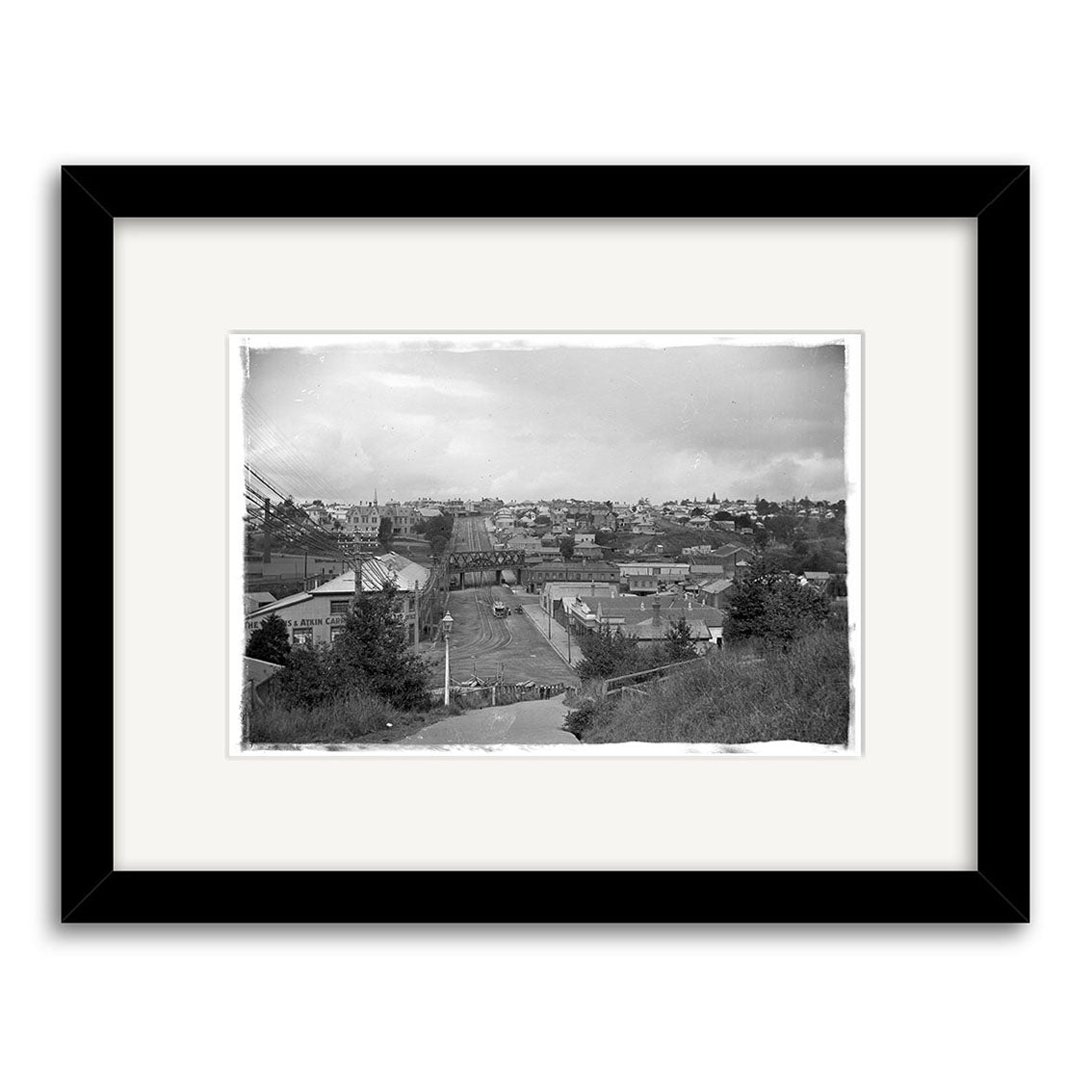 Parnell 1909 - HI052: Framed black-and-white historical photographic print of a small town cityscape with buildings and trees under a cloudy sky, viewed from above. Printed on archival quality matte paper for lasting beauty.
