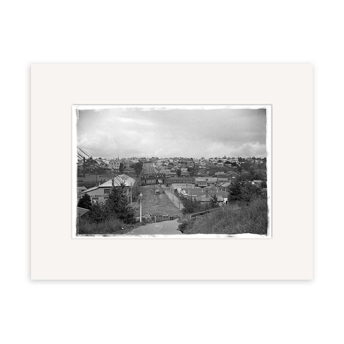 Black and white photo Parnell 1909 - HI052 shows a small town on a hillside under a cloudy sky, bordered by a white mat frame. Printed on archival-quality matte paper for an authentic historical photographic print look.