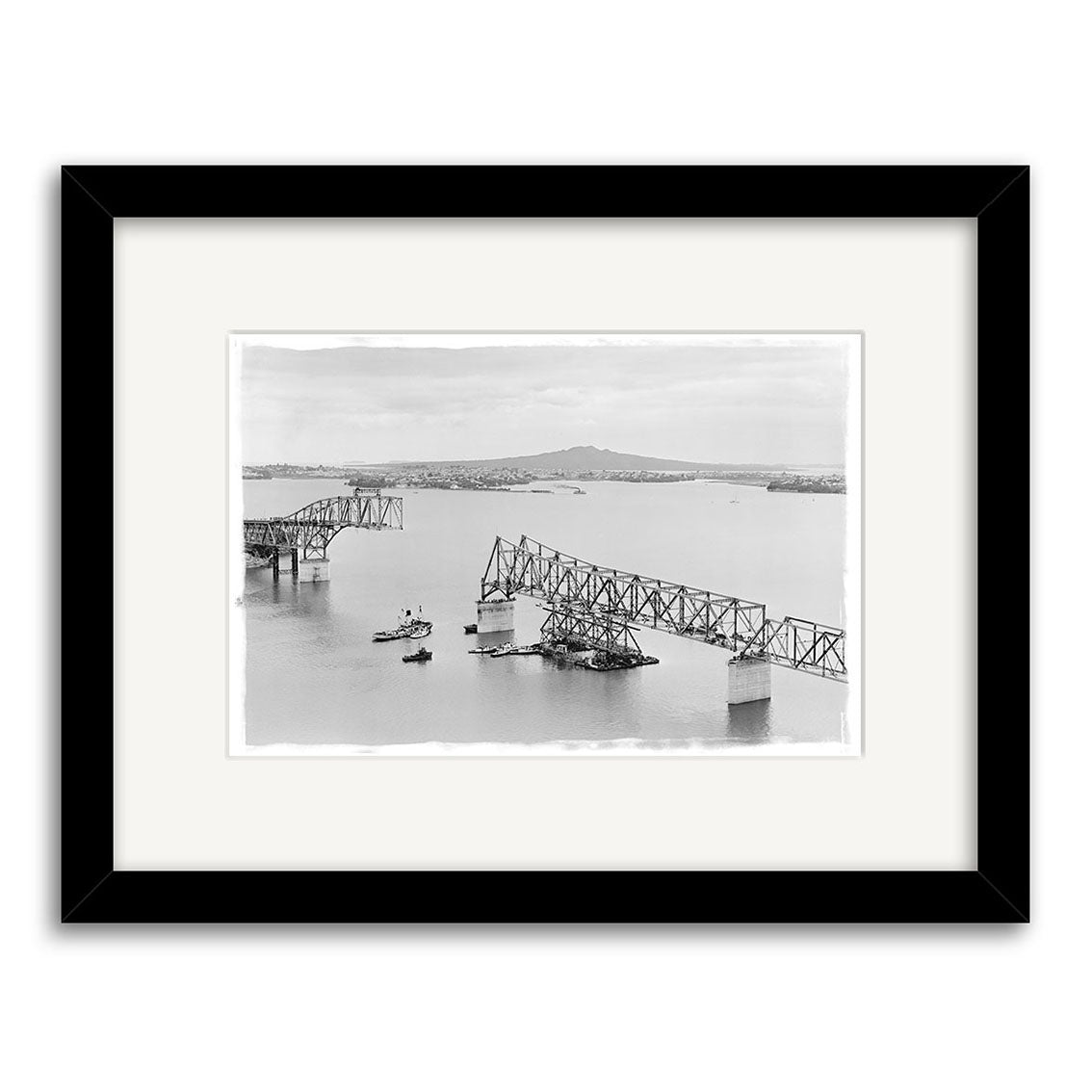 The HarbourBridge 1958 - HI054: a black-and-white historical print of a partially collapsed bridge over water, two center sections missing, boat nearby. Framed with white mat & black frame, printed on archival quality matte paper.