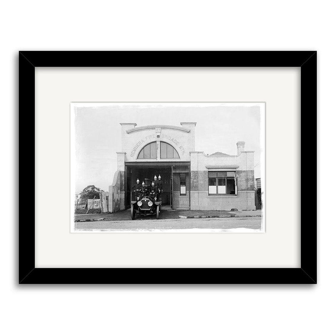 Remuera Fire Station 1920 - HI056: Black and white historical print of a vintage fire station with an old firetruck, framed with a white mat and black border on archival quality matte paper, highlighting the arched lettering above the entrance.
