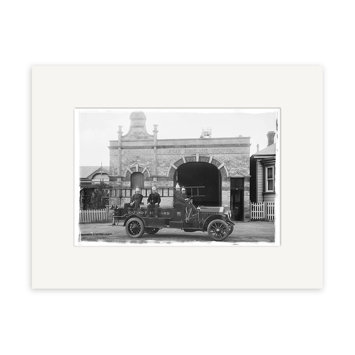 A vintage black-and-white photographic print, Ponsonby Fire Station 1919 - HI057, shows three men in an old-fashioned fire vehicle parked in front of the historic Ponsonby Fire Station with arched windows and ornate details.