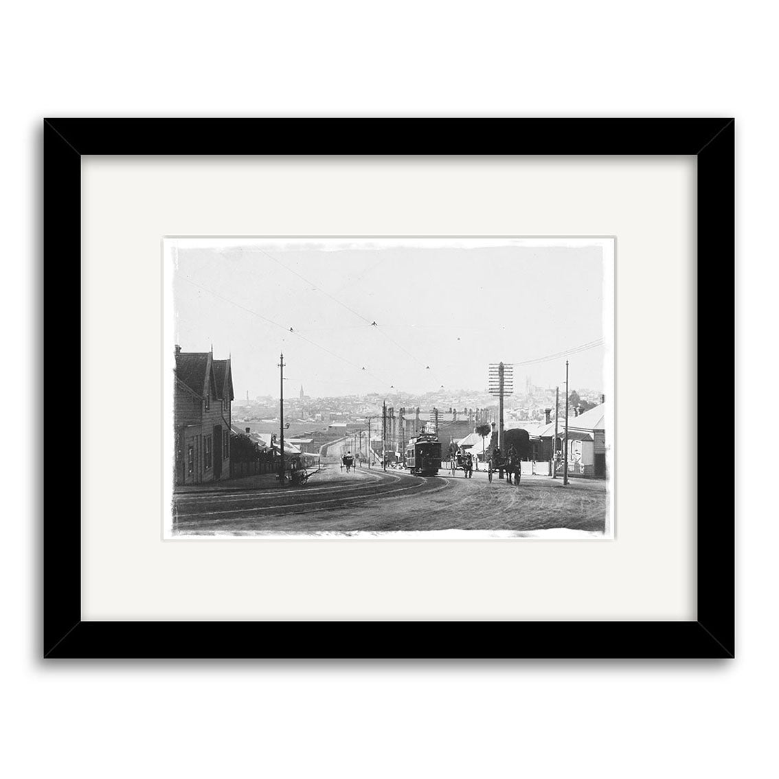 Black-and-white historical photographic print College Hill 1905 - HI061 showing a street scene in old New Zealand with horse-drawn carriages, people, houses, power lines, and a tramcar; archival-quality matting and black frame.