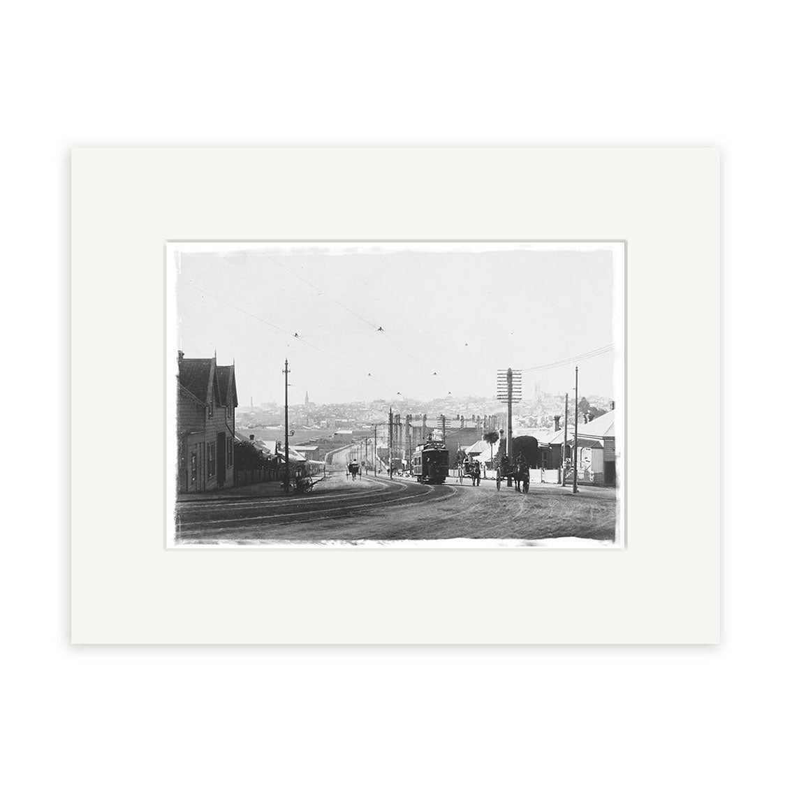 A black-and-white historical print, College Hill 1905 - HI061, depicts a New Zealand street with trolley tracks, horse-drawn carriages, utility poles, houses on both sides, and several people against a townscape backdrop.
