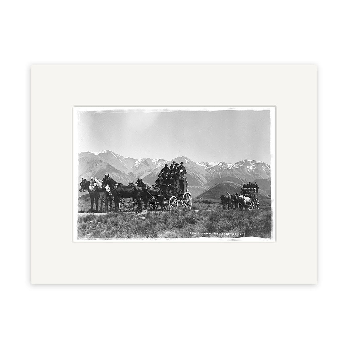 Archival quality black and white photo, Christchurch Rd Cass 1900 - HI062, shows two horse-drawn stagecoaches with several people aboard crossing a New Zealand plain, snow-capped mountains in the background.