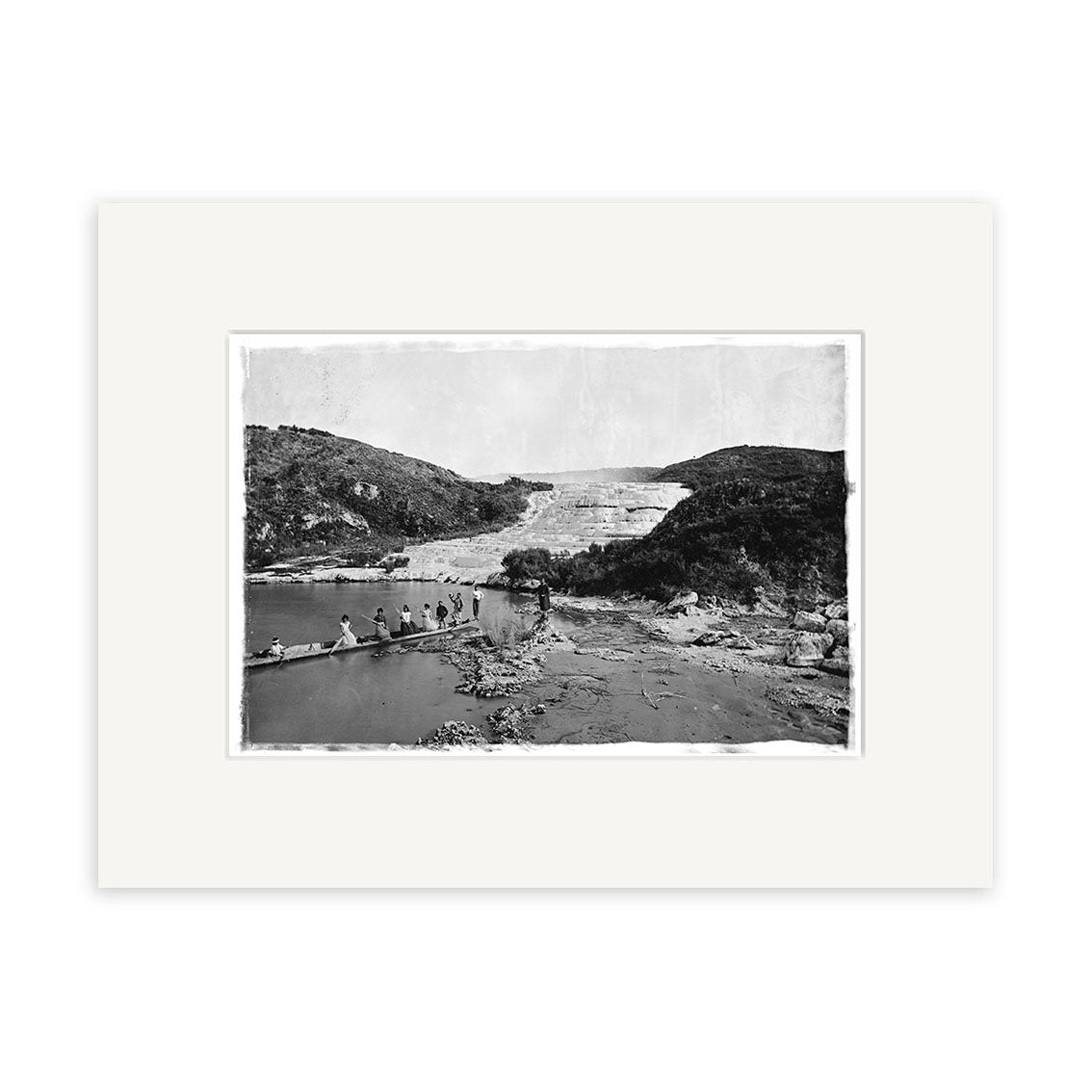 This archival-quality historical print, Pink Terraces 1879-1886 - HI064 from New Zealand, shows a group crossing a wooden bridge over water with rocky hills and a large geothermal terrace in the background. Wide white mat included.