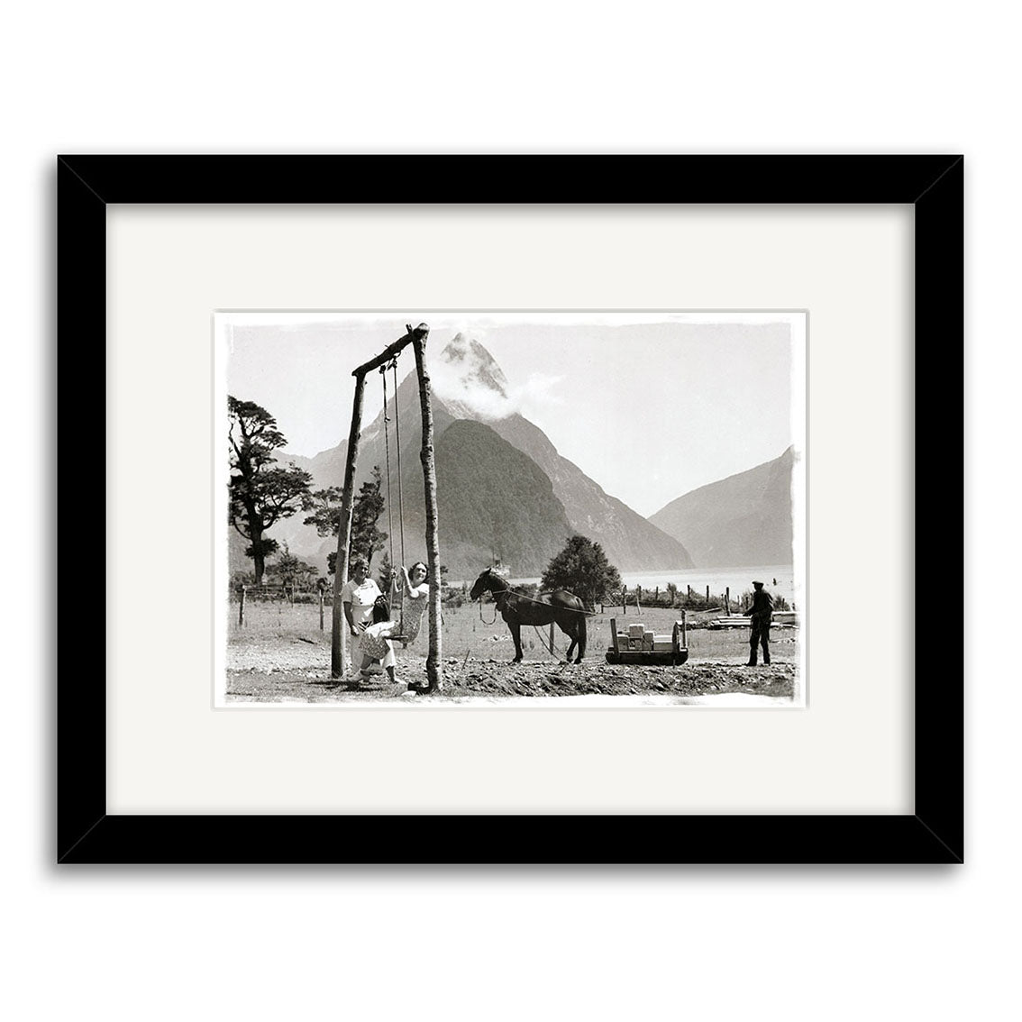 Black-and-white historical photo Milford Sound 1930 - HI067 shows three men and a horse near a wooden structure in a mountainous New Zealand landscape, with trees and mountains visible in the background.