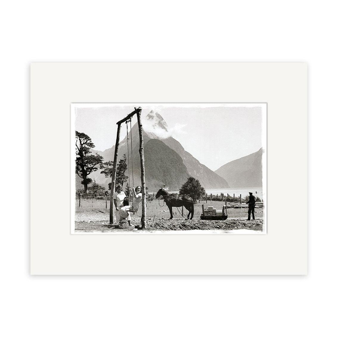 A black-and-white photo titled Milford Sound 1930 - HI067 shows two people and a horse by a wooden frame outdoors, with a man beside a cart and mountains with a cloud-covered peak in the background. Archival quality historical print.