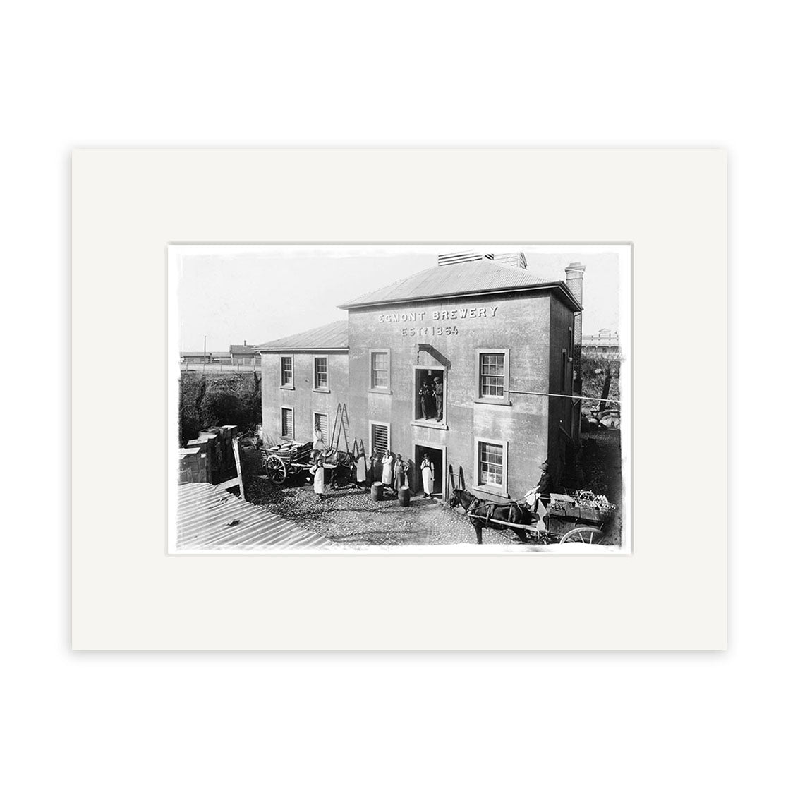 Black-and-white historical photographic print titled Overlook New Plymouth 1875 - HI068, featuring a two-story building with people, carts, and barrels outside—printed on archival quality matte paper.