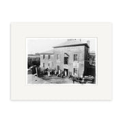 Black-and-white historical photographic print titled Overlook New Plymouth 1875 - HI068, featuring a two-story building with people, carts, and barrels outside—printed on archival quality matte paper.