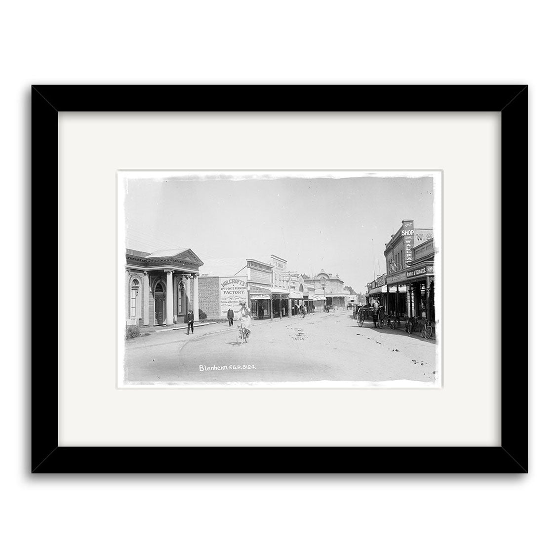 Black-and-white archival photographic print, Alfred Street 1911 - HI070, shows a small New Zealand town street with storefronts, pedestrians, and a horse-drawn carriage. Presented with a white mat and black border for quality display.