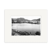 Picton 1890 - HI084: Black and white historical photographic print of a lakeside town with boats, people, and hillside buildings. Framed with a white mat on archival-quality matte paper for lasting beauty.