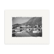 Picton Harbour 1930 - HI088: Black and white photo of a waterfront town with boats, buildings on shore, and mountain backdrop, centered with a white border on archival matte paper.