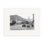 Archival quality Historical Photographic Print: High Street Picton 1910 - HI091 shows a black and white view of a wide street in small-town New Zealand, early 1900s cars parked along buildings, people nearby, and a mountain backdrop.