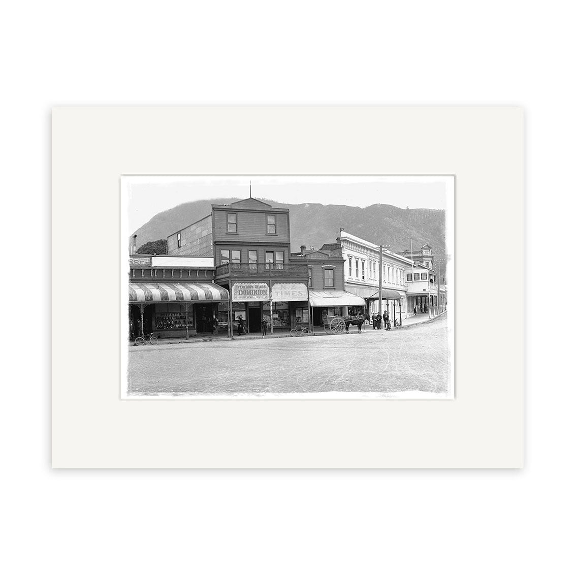 London Quay Picton 1910 - HI093: Black-and-white historical photographic print of historic storefronts and mountains with a horse-drawn carriage and pedestrians, made in New Zealand on archival quality paper.