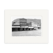 London Quay Picton 1910 - HI093: Black-and-white historical photographic print of historic storefronts and mountains with a horse-drawn carriage and pedestrians, made in New Zealand on archival quality paper.