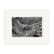 The Alexandra 1956 - HI102 is a matte black-and-white aerial photo featuring a winding river, rocky hills, buildings, roads, and bridges. This historic print comes framed with a wide white mat for archival-quality display.