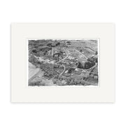 Arrowtown 1951 - HI106 is a black-and-white aerial photo of a small New Zealand town, depicting streets, buildings, fields, and trees. This historic print is on archival quality matte paper with a white border.