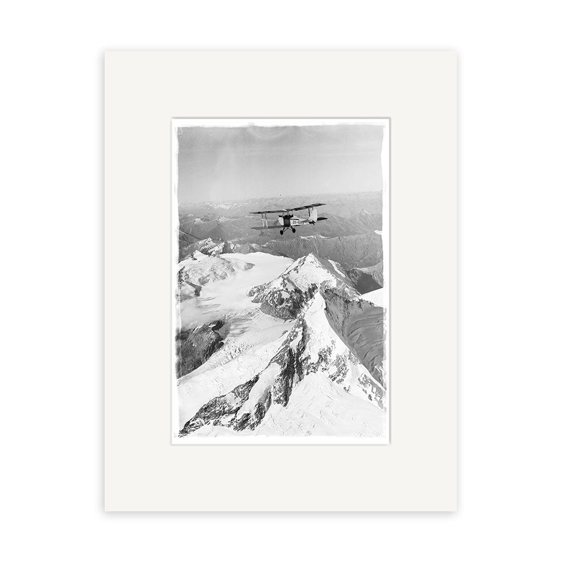 A black and white photograph, Mt Aspiring 1950 - HI107, shows a biplane above snow-covered peaks. Presented as a historical print, it is beautifully framed with a white mat on archival-quality matte paper.