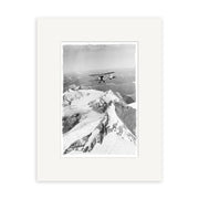 A black and white photograph, Mt Aspiring 1950 - HI107, shows a biplane above snow-covered peaks. Presented as a historical print, it is beautifully framed with a white mat on archival-quality matte paper.