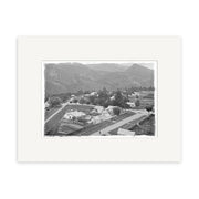 A black and white photograph titled Arrowtown 1926 - HI109 shows a rural New Zealand town with houses, roads, trees, and mountains. This historical print is framed with a wide white mat.