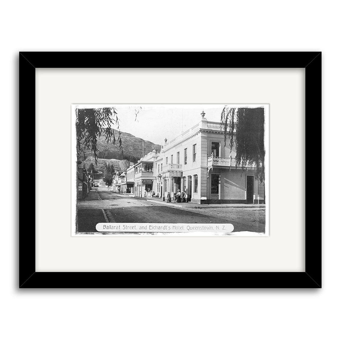 Black and white historical photographic print, Balarat St 1890 - HI112, shows Ballarat Street and Eichardts Hotel in Queenstown, NZ, with historic buildings and hills; framed in black with a white mat for archival quality.