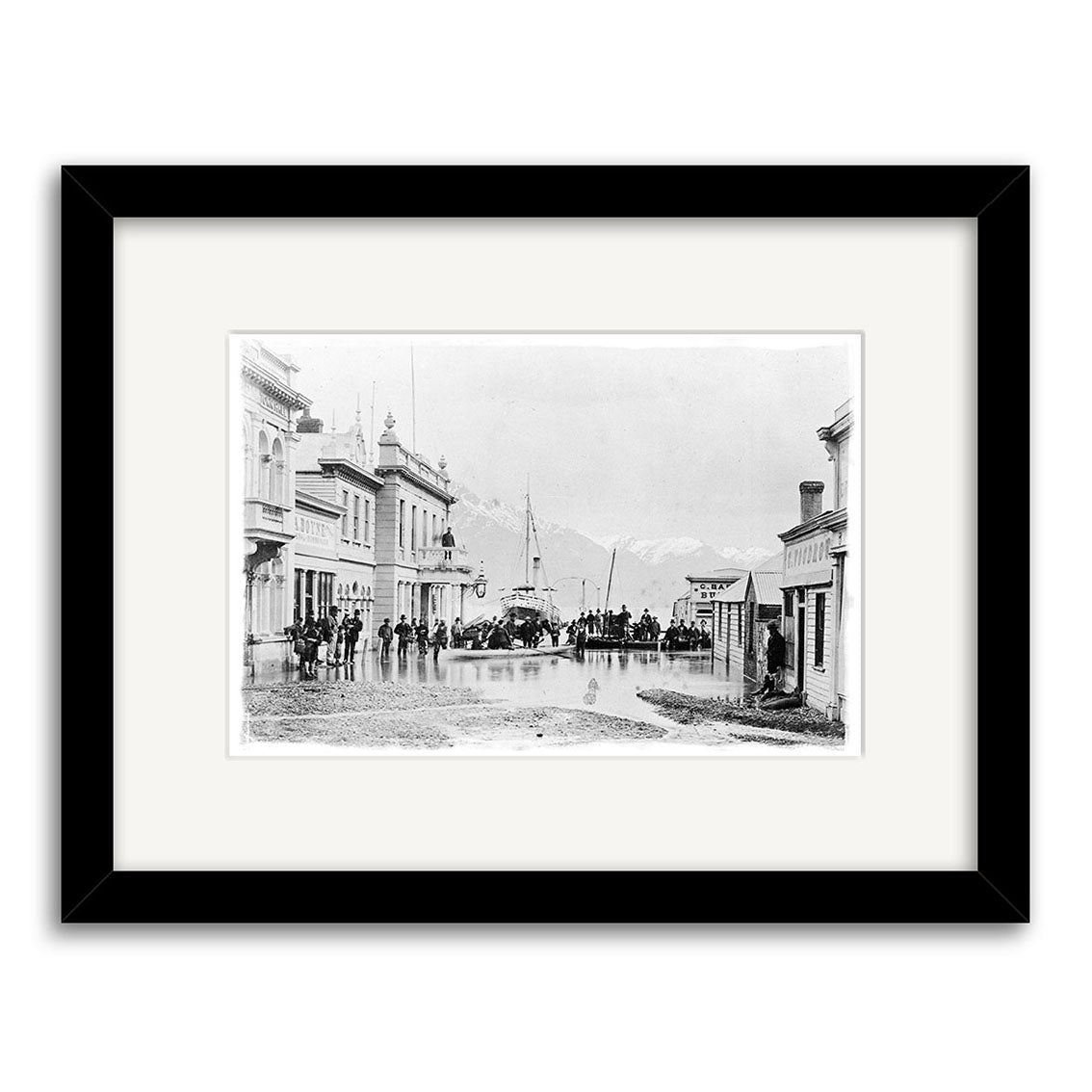 Archival quality black and white photographic print: Ballarat St Queenstown 1878 - HI113 depicts a New Zealand street scene with groups near buildings, a horse-drawn carriage, ship in the background, and faint mountains.