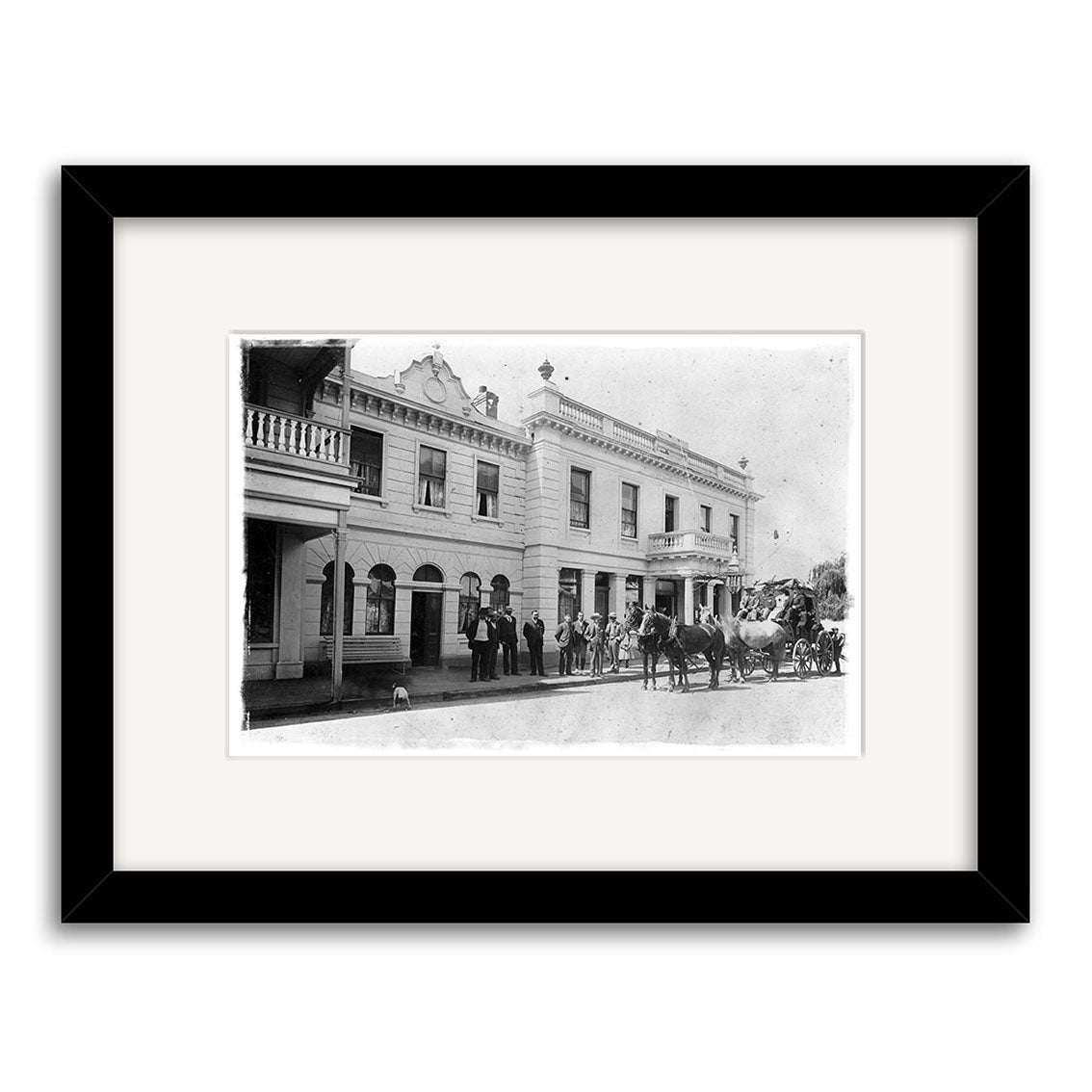 Archival quality black-framed, white-matted print: Cromwell coach leaving Eichardts Hotel, Ballarat Street, Queenstown, 1902 – HI115. Features a two-story building with arches, people, and a horse-drawn carriage in New Zealand.
