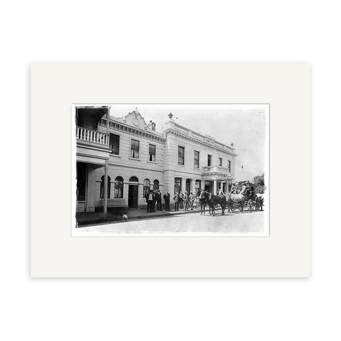 Archival quality black-and-white photo: “Cromwell coach leaving Eichardts Hotel, Ballarat Street, Queenstown, 1902 – HI115.” Features a two-story New Zealand building with arched windows, men in suits, and a horse-drawn carriage.