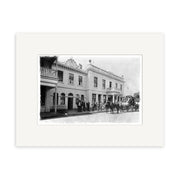 Archival quality black-and-white photo: “Cromwell coach leaving Eichardts Hotel, Ballarat Street, Queenstown, 1902 – HI115.” Features a two-story New Zealand building with arched windows, men in suits, and a horse-drawn carriage.