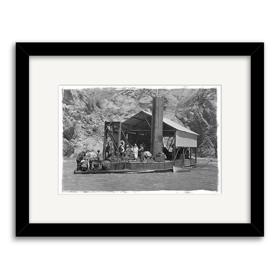 Black and white historical photographic print Golddredge 1930 - HI119 shows people on a wooden raft by rocky cliffs. Printed on archival matte paper and elegantly framed with a black frame and white mat.