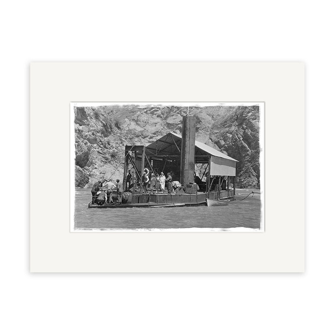 Black and white photo, Golddredge 1930 - HI119, shows people on a wooden ferry crossing a river with rocky cliffs behind. Printed on matte paper, this historical print highlights the ferry’s canopy and central support structure.
