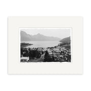 Black-and-white photo Queenstown 1905 - HI123: a calm New Zealand lakeside town with buildings, trees, and mountains. Historical photographic print, matted with a white border on archival-quality matte paper.