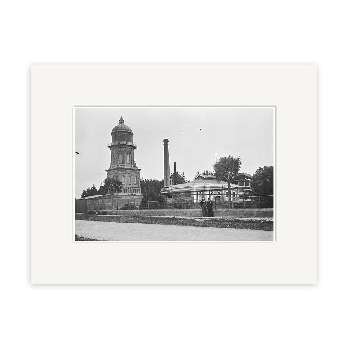 The Water Tower 1925 - HI124 is a black and white photo featuring a domed building, tall smokestack, and people near a stone wall amid trees, showcasing a New Zealand streetscape in high archival quality.