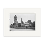 The Water Tower 1925 - HI124 is a black and white photo featuring a domed building, tall smokestack, and people near a stone wall amid trees, showcasing a New Zealand streetscape in high archival quality.