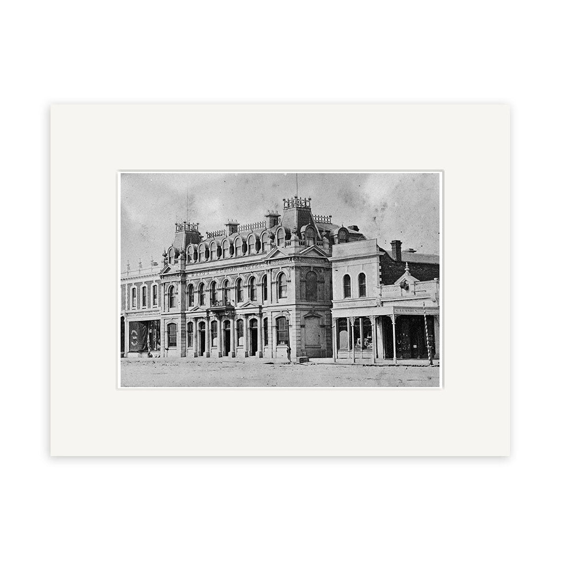 A black-and-white vintage photograph of Mayos Albion Hotel 1877 (HI125), showcasing its ornate multi-story architecture and chimneys in New Zealand, is framed with archival quality matte paper; the historic print features an empty street in front.