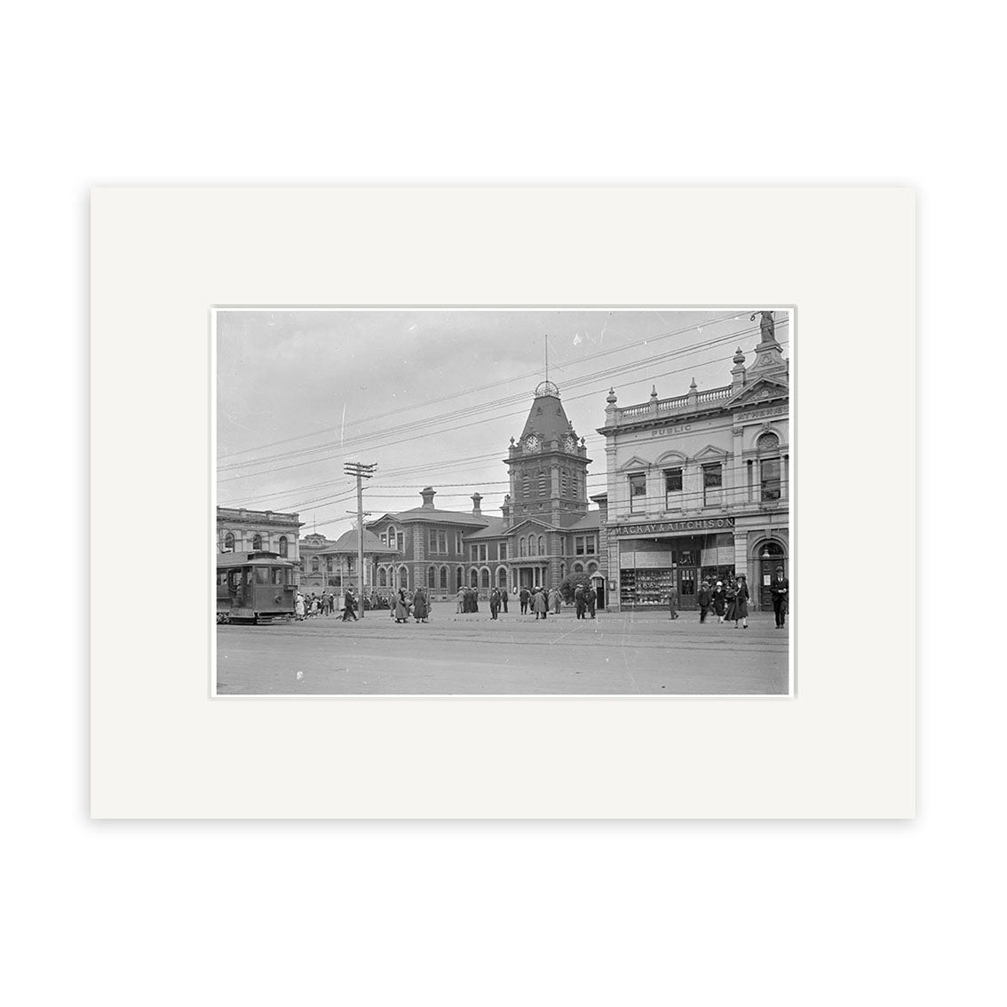 Black and white historical print Post Office 1925 - HI126 shows a tranquil New Zealand town square with a tram, people, clock tower, and ornate buildings. Printed on archival matte paper for lasting beauty.