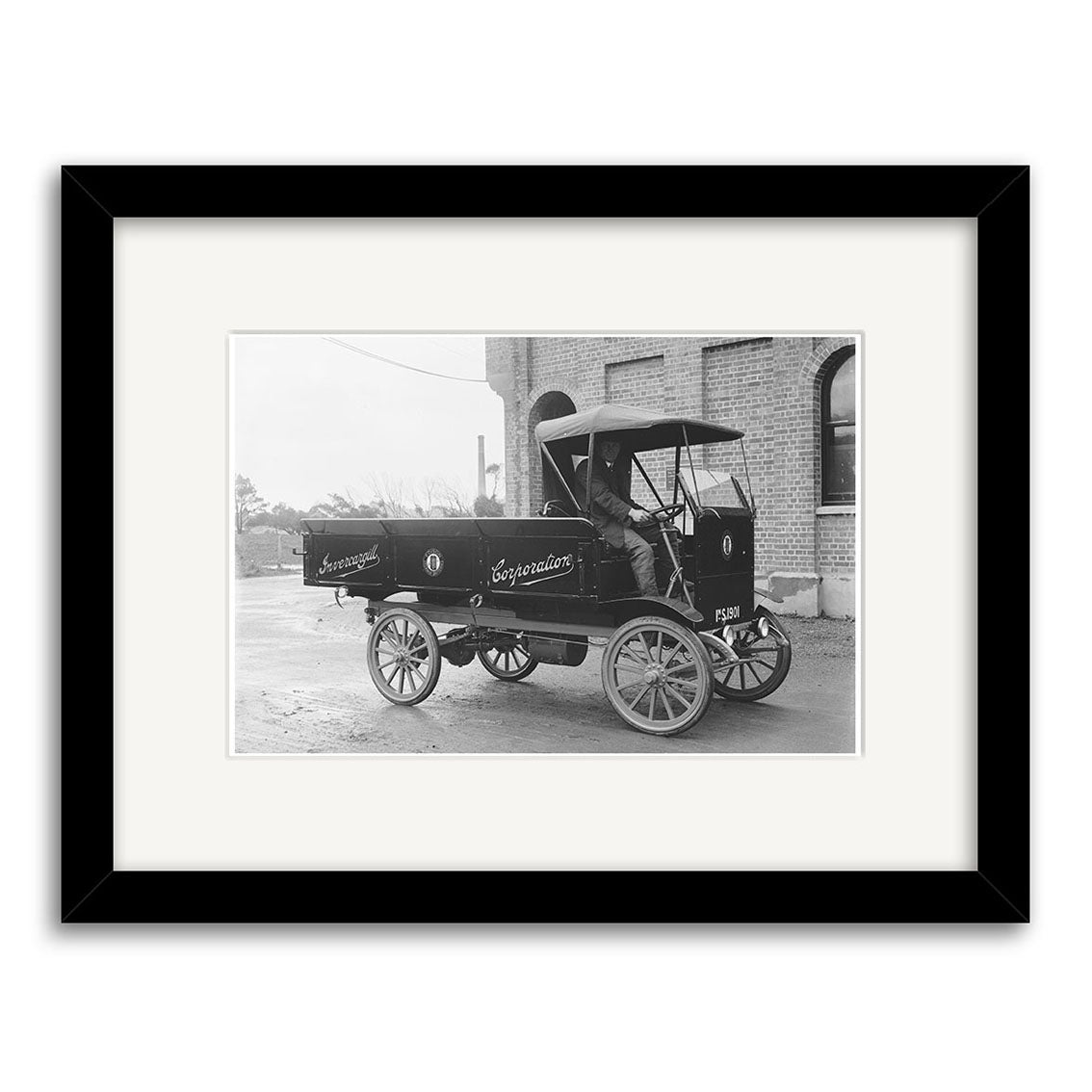 A black-and-white historical photographic print titled Electric Truck Invercargill 1920 - HI127 shows an early electric delivery truck by a brick building. The image is framed in black with a white mat and printed on archival quality paper.