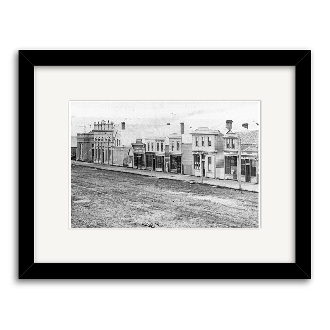 Black-and-white historical print Tay St 1864 - HI128 shows old-fashioned storefronts on an unpaved street. Printed on archival quality matte paper, it is framed with a white mat and black frame.