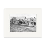 Historical black and white photograph Tay St 1864 - HI128 shows a row of commercial buildings on an unpaved street in a historic town. No vehicles or people are present. Printed on archival quality matte paper for lasting beauty.