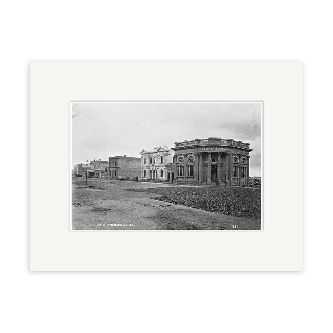 Tay Street 1880 - HI129 is a black and white historical photographic print of a dirt street in New Zealand lined with brick buildings, featuring columns and an arched facade. The archival quality image shows an empty, tranquil scene.