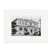 Black and white photo of a two-story classical building with arched windows, columns, and vintage cars out front. Palm trees line the side in this historical print: Govt Building 1922 - HI131, made in New Zealand.