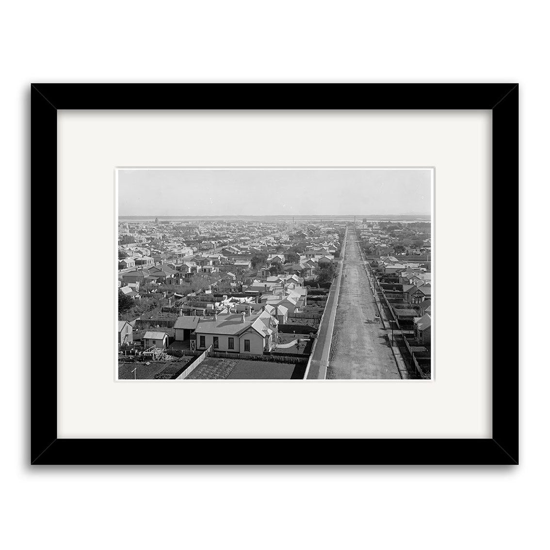 Black and white photograph titled Invercargill 1900 - HI132 depicting a cityscape with a long, straight street lined with houses. Printed on archival quality paper and elegantly framed with a white mat and black frame. Made in New Zealand.