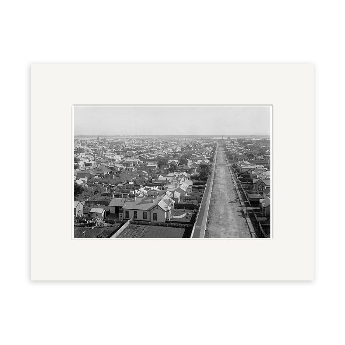 Black and white aerial photograph titled Invercargill 1900 - HI132 shows a long, straight road lined with houses and buildings under a clear sky. This historical photographic print is made in New Zealand.