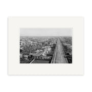 Black and white aerial photograph titled Invercargill 1900 - HI132 shows a long, straight road lined with houses and buildings under a clear sky. This historical photographic print is made in New Zealand.
