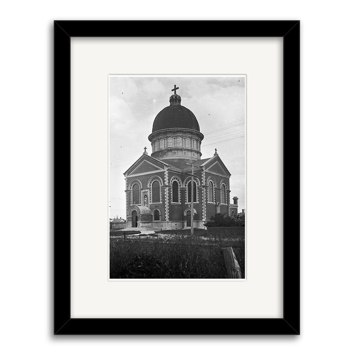 Black and white photo of Stmarys Basilica (1925) with dome, arched windows, and cross, surrounded by a fence. Displayed in a black frame with white mat, HI136 celebrates New Zealands rich architectural heritage.