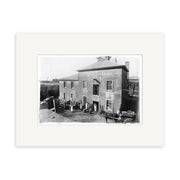 Archival-quality black and white historical photo print of Egmont Brewery 1906 (HI138), showing a two-story building in New Zealand with people, carts, gardening tools, a fence, and trees in the background.