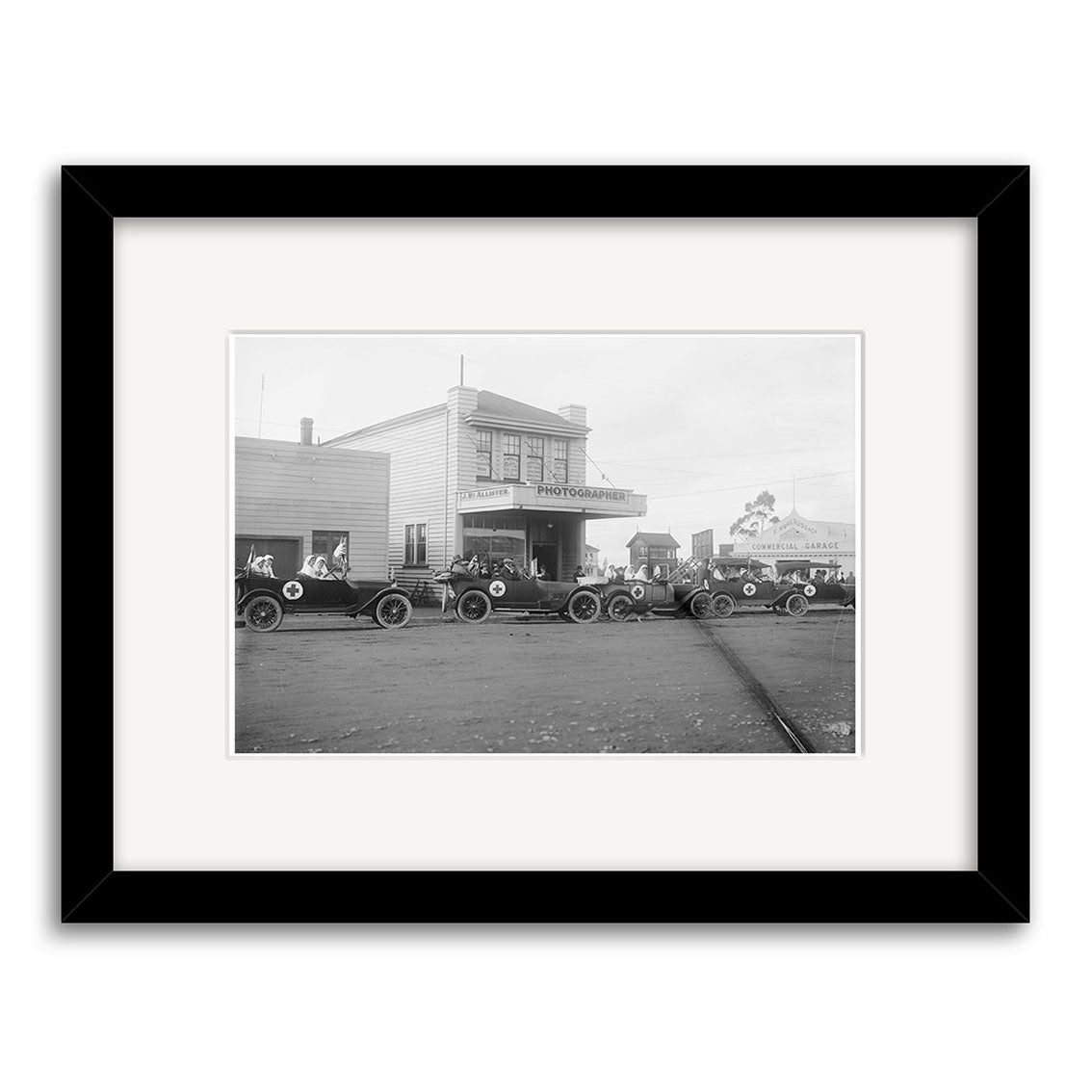 Black and white photo titled Broadway Stratford 1919 - HI139 shows vintage cars on a dirt road before a two-story Photographer building. Printed on archival quality matte paper, it captures the historical charm of New Zealand.