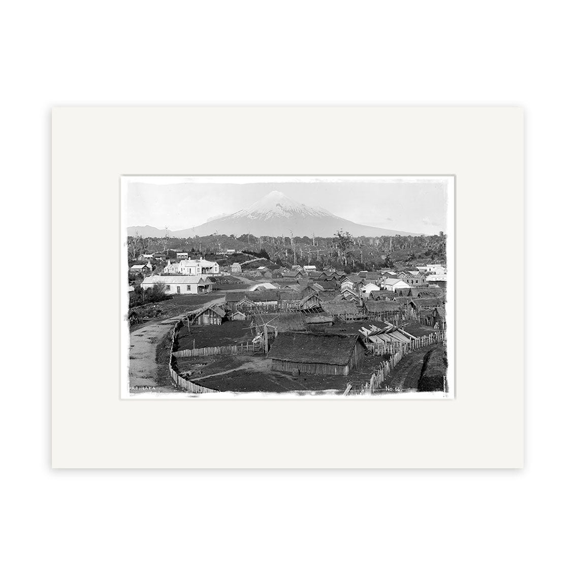 A black-and-white historical photographic print, Mount Taranaki 1890 - HI142, shows a village with thatched and wooden buildings in the foreground and a snow-capped mountain behind, framed by archival quality matte paper.