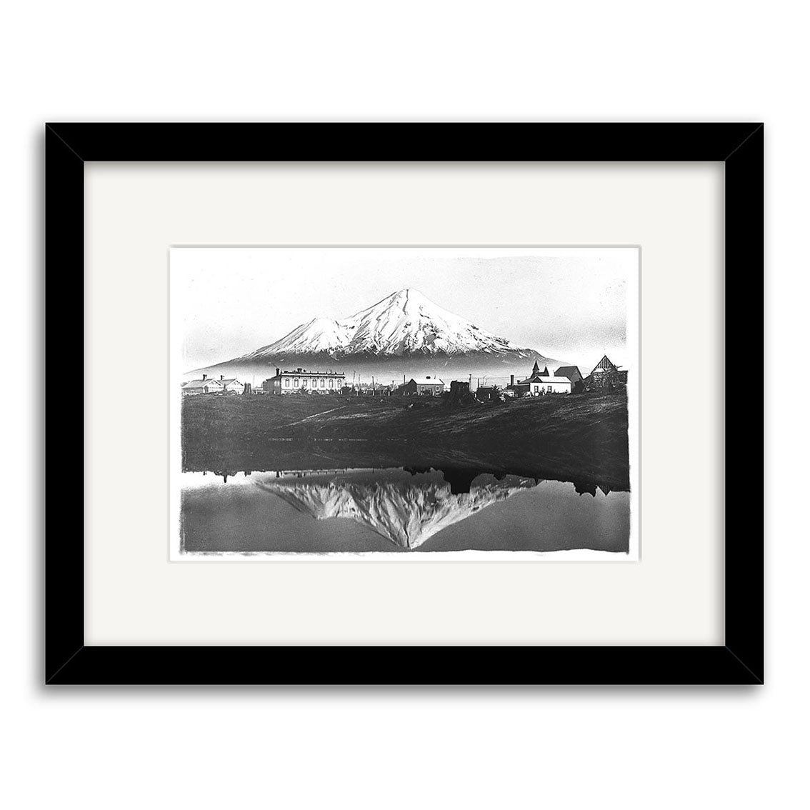 Mt Taranaki 1900 - HI144: Black and white drawing of a mountain with buildings at its base reflected in water. Inspired by New Zealand, this artwork is framed with a white mat and black border on archival quality paper.